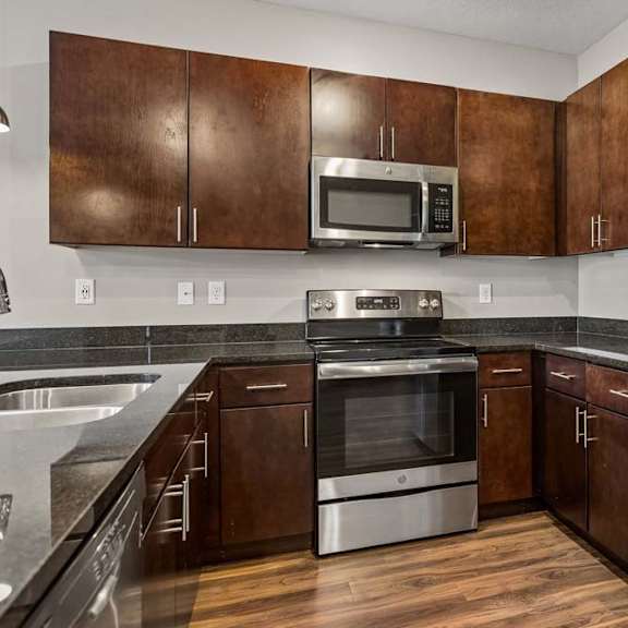 Thumbnail 6 of 18 Contemporary kitchen with dark wood cabinetry, stainless steel appliances, tile backsplash, and wood-look flooring.