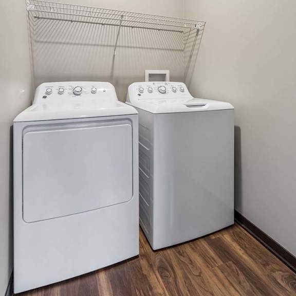 Thumbnail 11 of 18 Laundry room with side-by-side washer and dryer, wire shelf storage, and neutral walls in an apartment home.