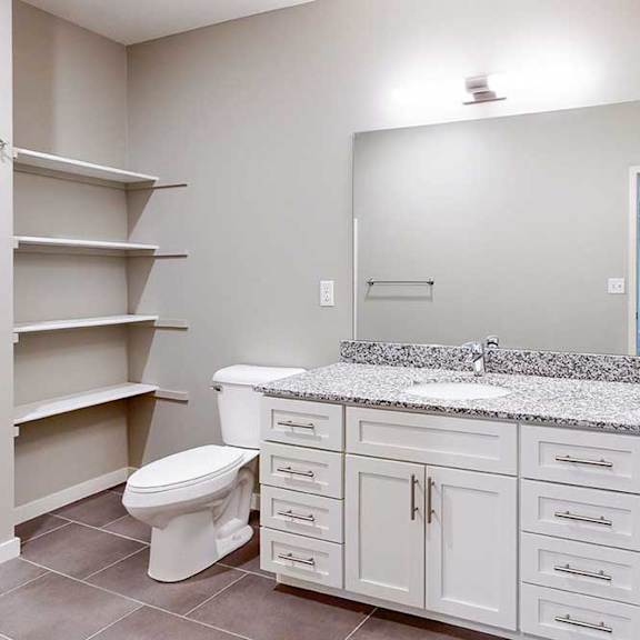 Thumbnail 19 of 26 A bathroom with a granite vanity, white wooden cabinets, a tall storage cabinet, an oversized mirror, and built-in linen shelves.