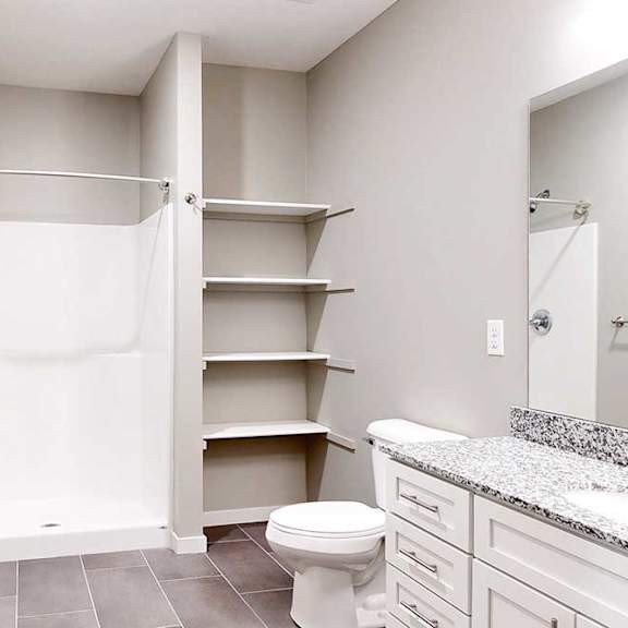 Thumbnail 6 of 26 A bathroom with a granite vanity, white wooden cabinets, built-in linen shelves, and a walk-in shower.
