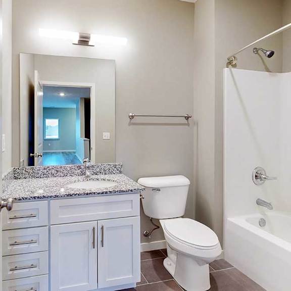 Thumbnail 13 of 26 A bathroom with a granite vanity, white wooden cabinets, and a tub shower.