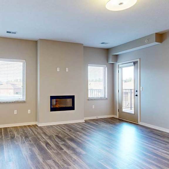 Thumbnail 8 of 26 A living room with hardwood-style flooring, large windows, an electric fireplace, and a windowed door to a balcony.