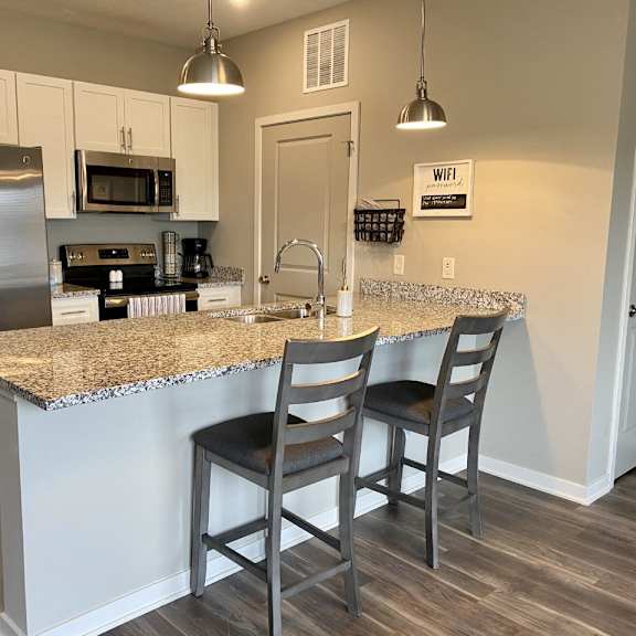 Thumbnail 3 of 16 A kitchen with a granite countertop and two chairs.