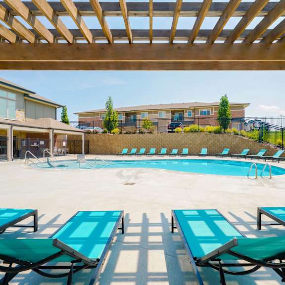 lounge chairs under a pergola overlooking a resort-style pool