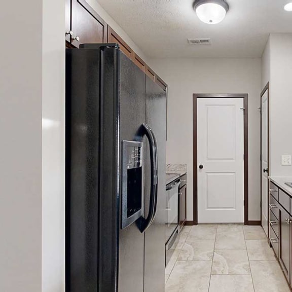 Thumbnail 6 of 22 a galley kitchen with granite countertops, dark cabinets, black appliances, a pantry, and a laundry room at the end