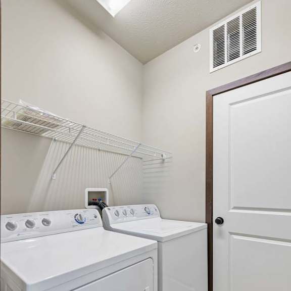 Thumbnail 14 of 30 In-home laundry room with white washer and dryer, wire shelving, neutral walls, and tile flooring.