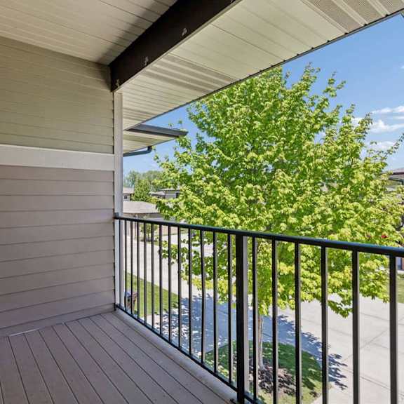 Thumbnail 24 of 40 Private apartment balcony with black railing, wood-look decking, and leafy community view.