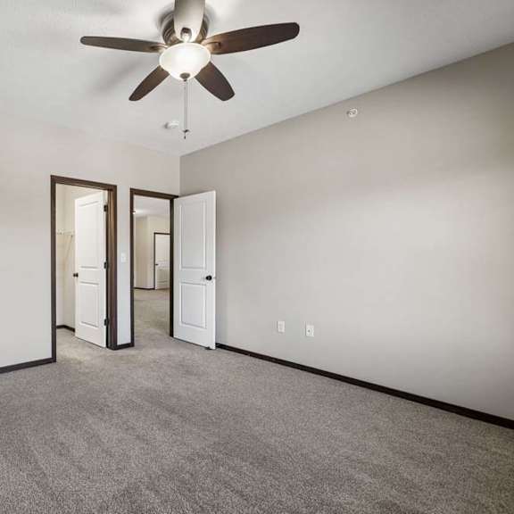 Thumbnail 31 of 40 Empty carpeted bedroom with ceiling fan, neutral walls, and doorways to the bathroom and hall.