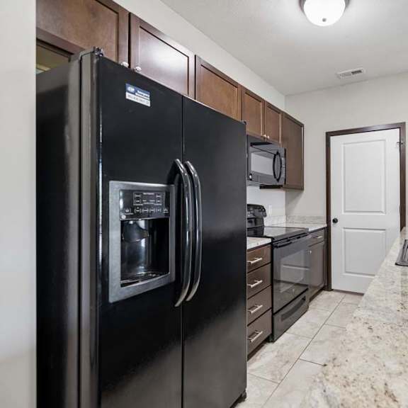 Thumbnail 18 of 19 A black refrigerator is in a kitchen with granite countertops.