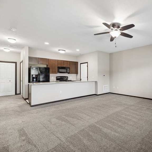 Thumbnail 2 of 19 Large carpeted living room with ceiling fan, wall fireplace, window with blinds, and front door.