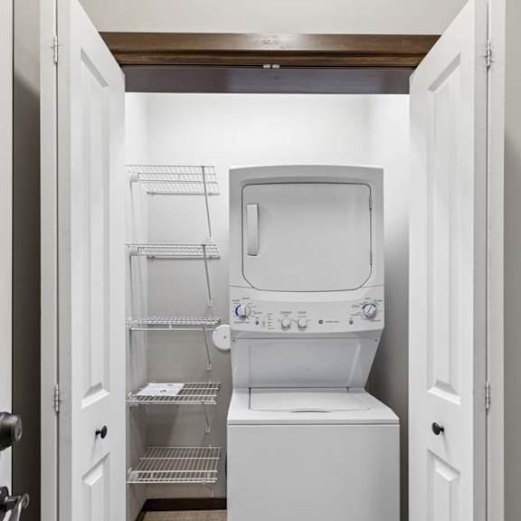 Thumbnail 16 of 19 Laundry closet with stacked washer and dryer, white wire shelving, and tile flooring.