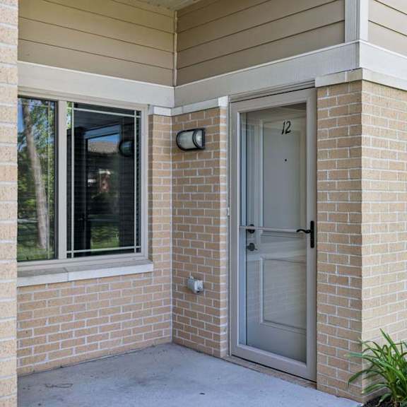 Thumbnail 4 of 19 Apartment exterior entry with brick walls, screened front door, large windows, and landscaped greenery.
