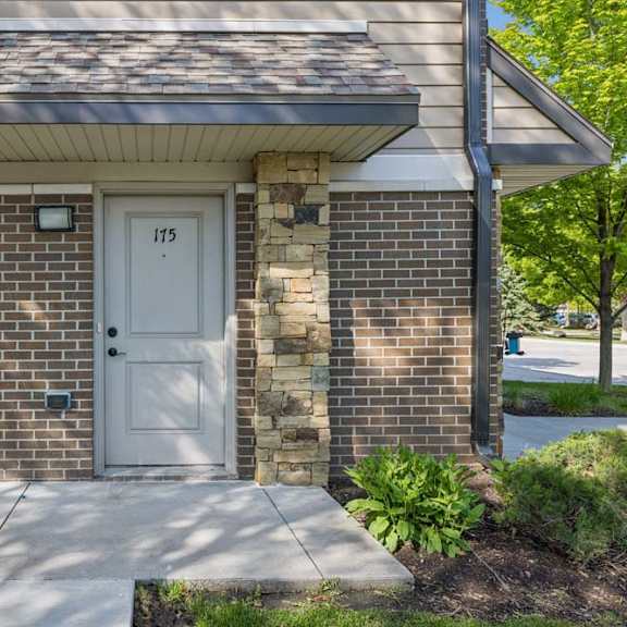 Thumbnail 2 of 16 Apartment exterior entry with brick facade, stone columns, unit door 175, sidewalk, and landscaped greenery.