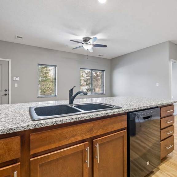 Thumbnail 6 of 16 Kitchen breakfast bar with double sink, dishwasher, wood cabinetry, and view into the living area.