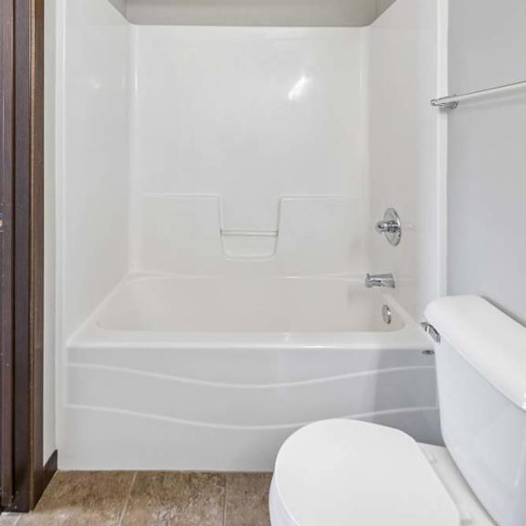 Thumbnail 47 of 48 Apartment bathroom with white tub shower combo, curved shower rod, tile flooring, towel bar, and toilet.