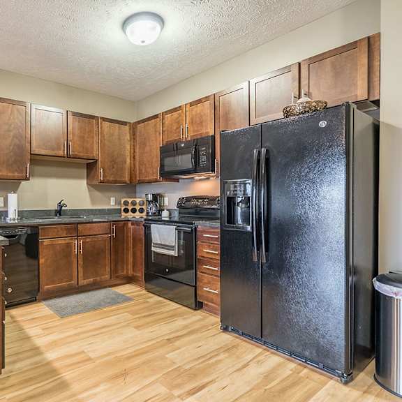 Thumbnail 4 of 15 A kitchen with a black refrigerator and warm, medium brown wooden cabinets.
