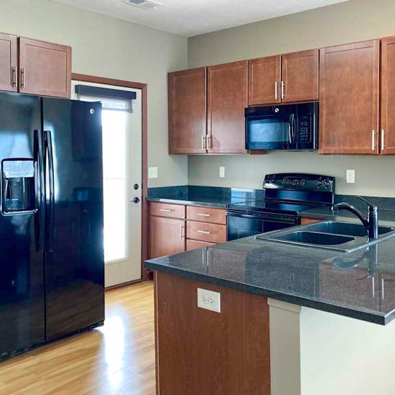 Thumbnail 9 of 16 A kitchen with wooden cabinets, dark granite countertops, black appliances, and a door to a balcony.