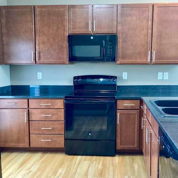 Thumbnail 8 of 16 A kitchen with wooden cabinets, dark granite countertops, and black appliances.