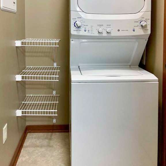 Thumbnail 16 of 16 A stacked full-size washer and dryer in a laundry room with built-in shelves.