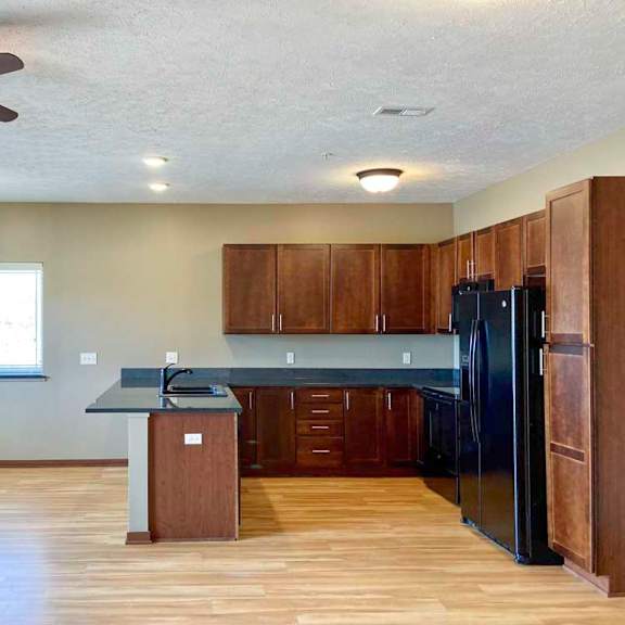 Thumbnail 5 of 19 A kitchen with granite countertops, wooden cabinets, black appliances, and a peninsula counter next to a dining area with windows.