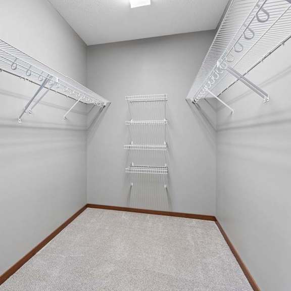 Thumbnail 12 of 16 Spacious apartment walk-in closet with neutral carpet and extensive white wire shelving along three walls.