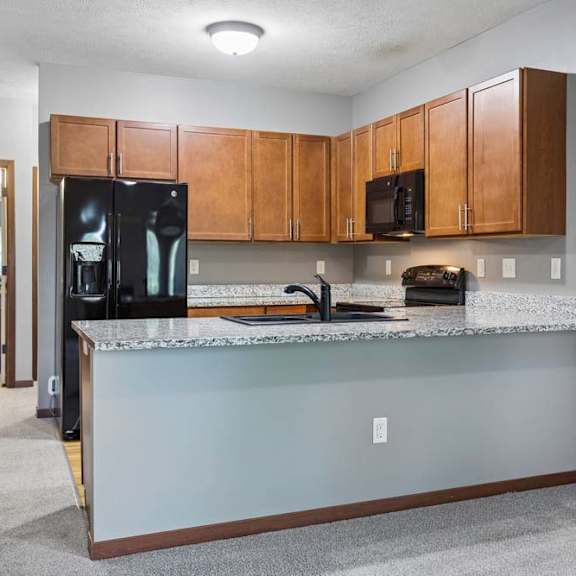 Thumbnail 5 of 16 Kitchen with warm wood cabinetry, granite countertops, black appliances, and a spacious breakfast bar.