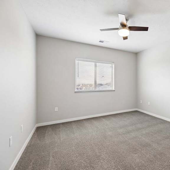 Thumbnail 36 of 44 Spacious apartment bedroom with carpeted flooring, a ceiling fan, neutral walls, and a window with blinds providing natural light.