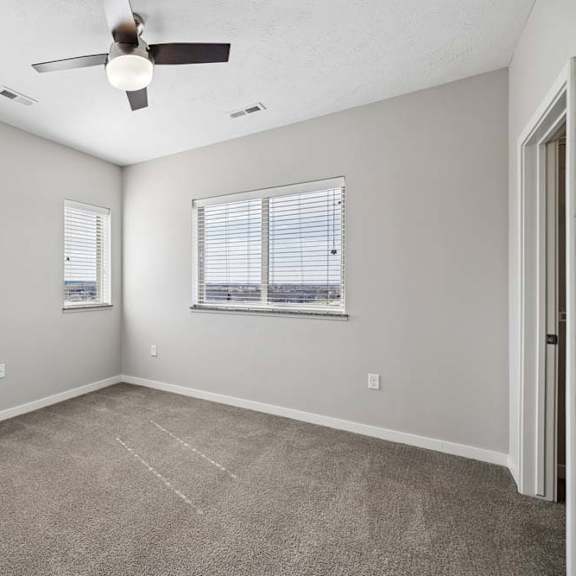 Thumbnail 35 of 44 Spacious apartment bedroom with carpeted flooring, a ceiling fan, two windows with blinds providing natural light, and a sliding closet door.