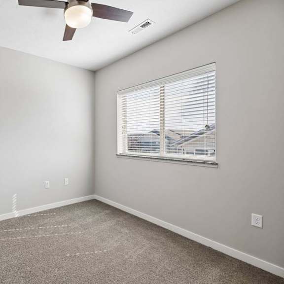 Thumbnail 34 of 44 Bright apartment bedroom with carpeted flooring, a ceiling fan, neutral walls, and a window with blinds providing natural light.