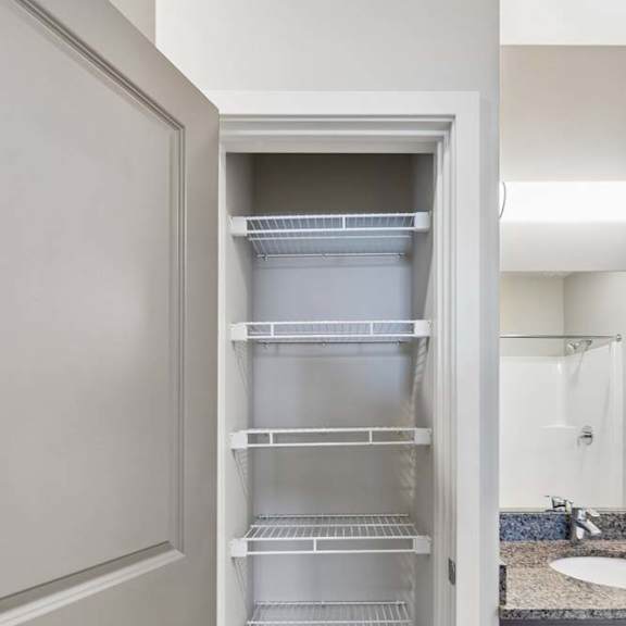 Thumbnail 33 of 44 Apartment linen closet with built-in wire shelving, wood-style flooring, and double doors, located beside the bathroom vanity for convenient storage.