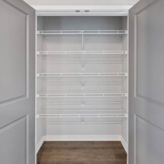 Thumbnail 32 of 44 Apartment closet with double doors, built-in wire shelving, hanging rods, and wood-style flooring for convenient storage.