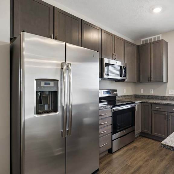Thumbnail 29 of 44 Modern apartment kitchen with dark cabinetry, granite-look countertops, stainless steel appliances, and a large window above the sink providing natural light.