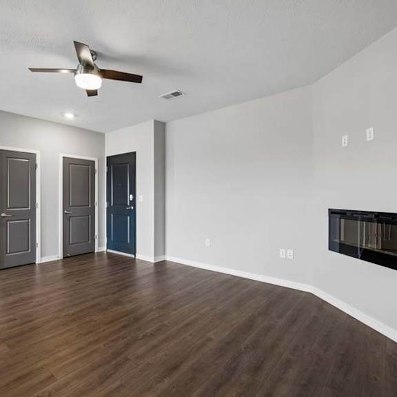 Thumbnail 30 of 44 Spacious apartment living room with wood-style flooring, a ceiling fan, a wall-mounted fireplace, and an open layout with multiple interior doors and abundant natural light.