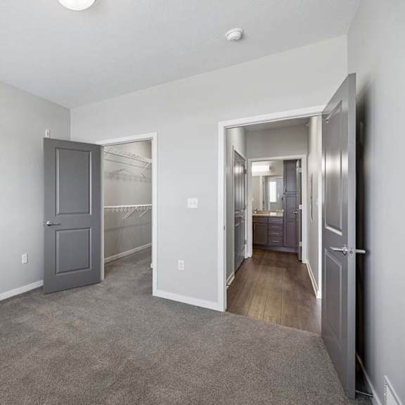 Thumbnail 18 of 36 Bright apartment bedroom with carpeted flooring, an open closet with sliding doors, gray interior doors, and access to the adjoining hallway.