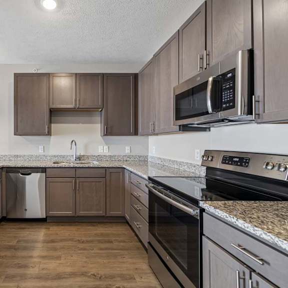 Thumbnail 21 of 36 Modern apartment kitchen with dark cabinetry, granite-look countertops, stainless steel appliances, and a spacious U-shaped layout with ample counter space and storage.