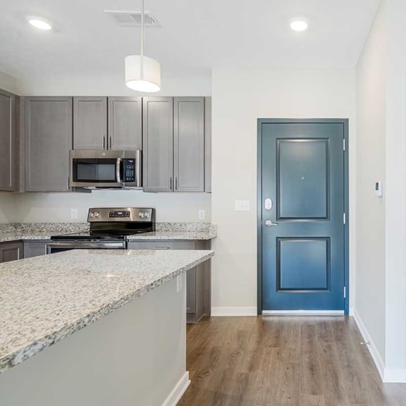 Thumbnail 2 of 19 an open-concept kitchen with gray cabinets and stainless steel appliances next to a front door
