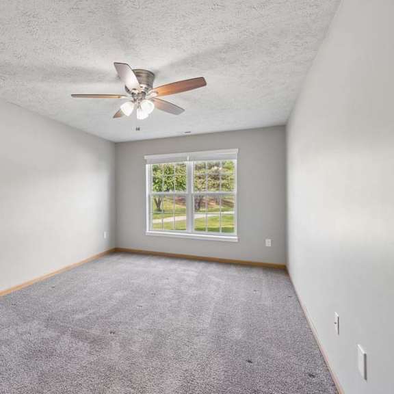 Thumbnail 8 of 13 Bright apartment bedroom with soft carpeting, a ceiling fan, and a large window providing natural light.