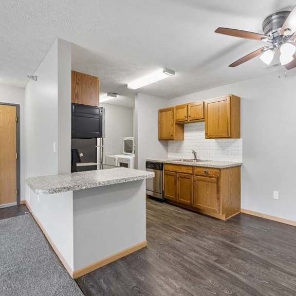 Thumbnail 4 of 13 Open apartment dining area with wood-style flooring, a breakfast bar, ceiling fan, and adjoining kitchen with wood cabinetry.