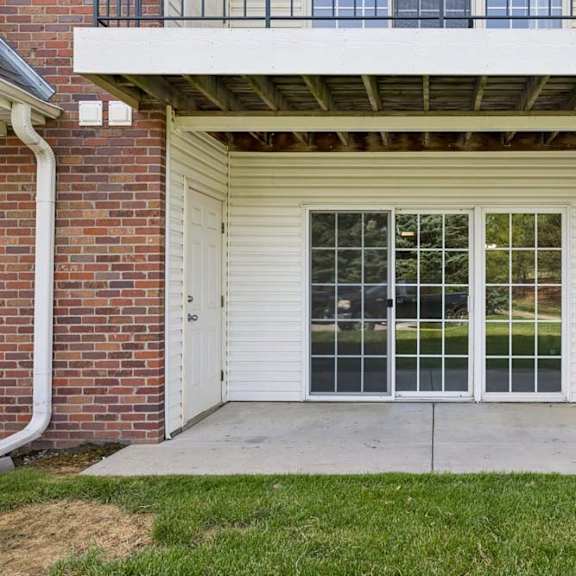 Thumbnail 13 of 13 Covered ground-floor apartment patio with a concrete seating area, sliding glass door, and grassy lawn.
