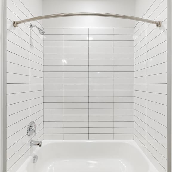 a white tiled bathroom with a white tub and a white shower curtain.