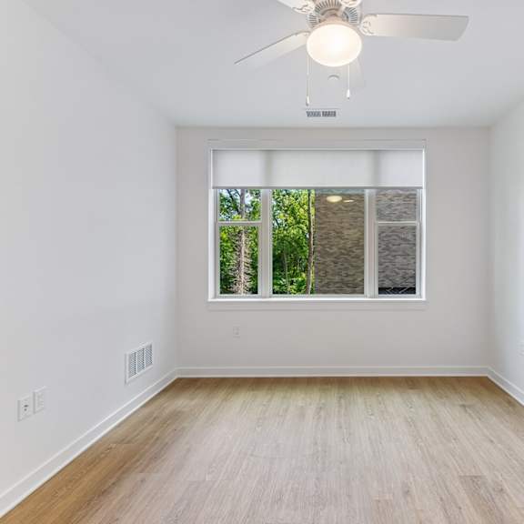 a room with a ceiling fan and a window with a view of trees.