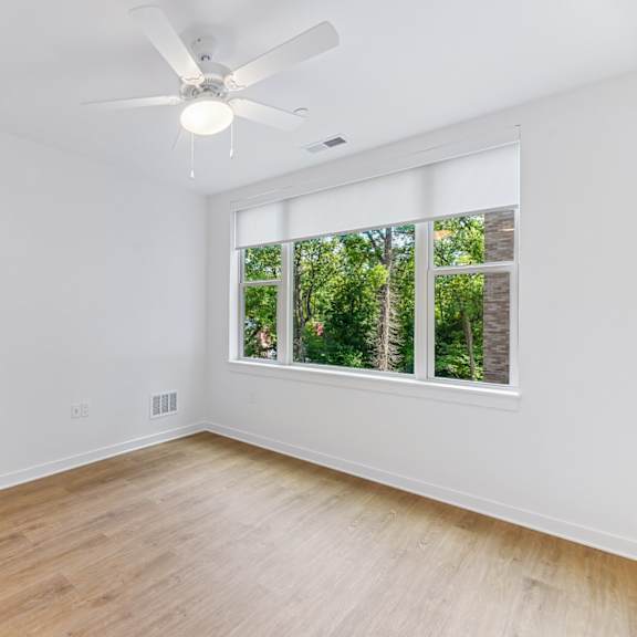 a room with a ceiling fan and a window overlooking trees.