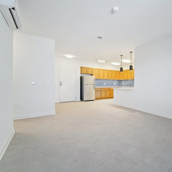 a large empty room with a kitchenette in the background.