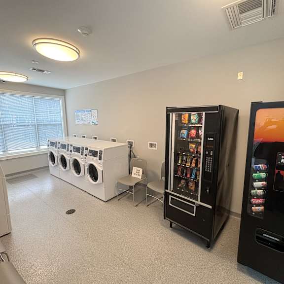a room with a washing machine, a vending machine, and a fridge.