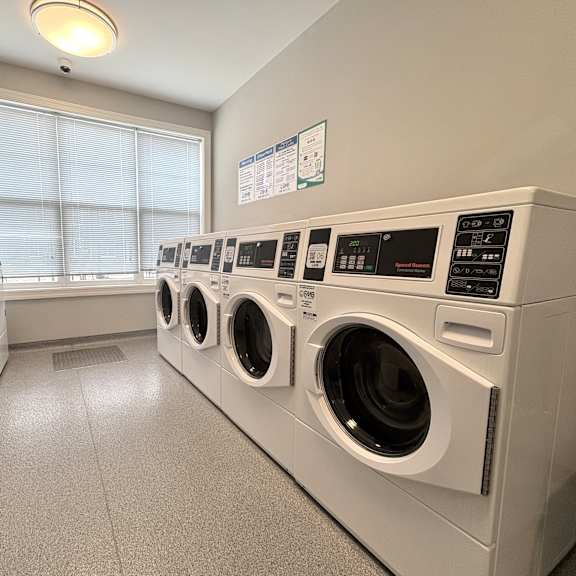 a row of white front load washing machines in a laundromat.