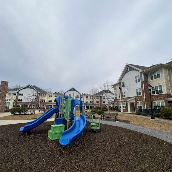 a playground with a blue and green slide in front of apartment buildings.