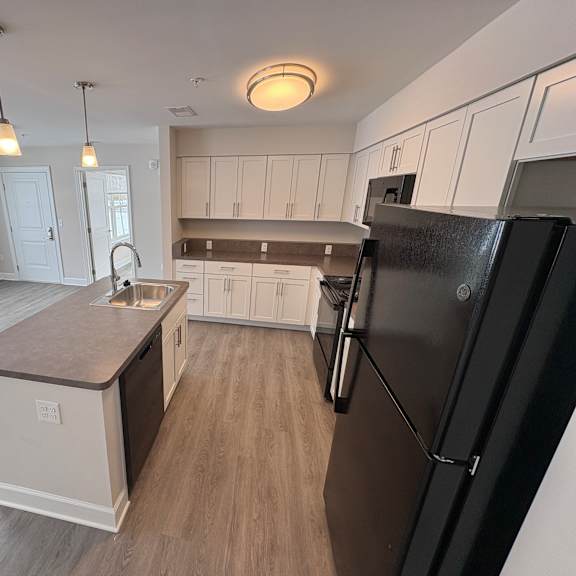 a kitchen with a black refrigerator and wooden floors.