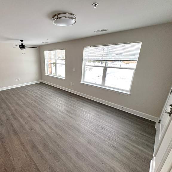 a room with a ceiling fan and two windows.