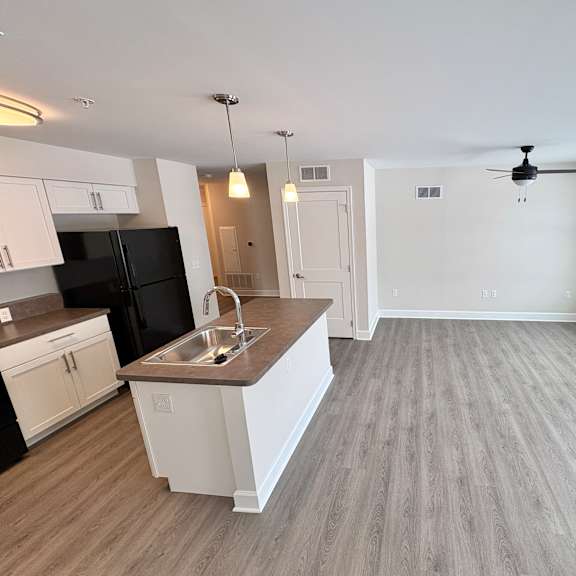 a spacious kitchen with a black refrigerator, white cabinets, and a wooden floor.