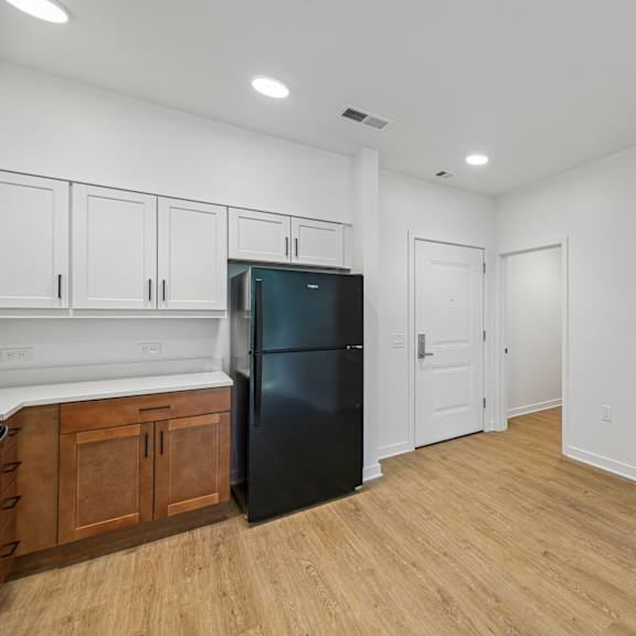 a black refrigerator sits in a kitchen with wooden floors and white walls.